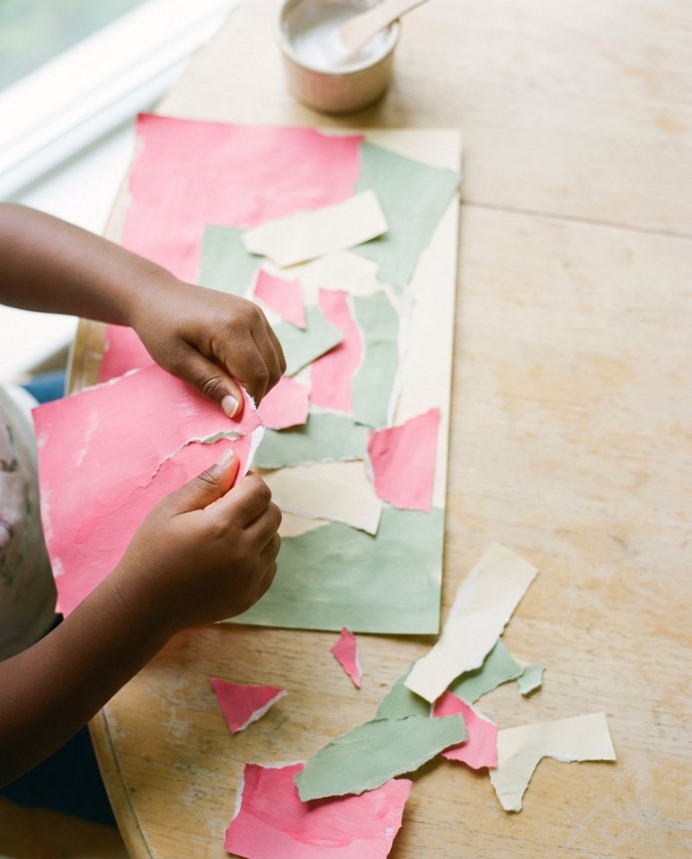 Deux mains déchirent une feuille peinte en rose pour composer un collage vert, rose et crème.